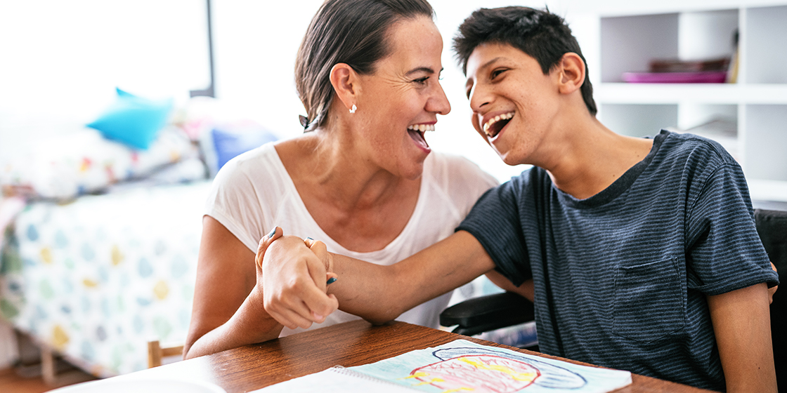 Mom and son smiling: son has a physical disability and is seated in a wheelchair.